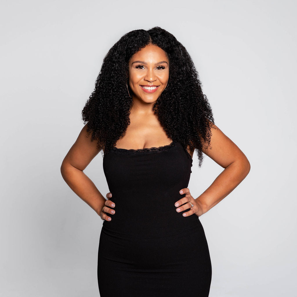 Studio portrait of a Portland lash educator and beauty entrepreneur wearing a fitted black dress, standing confidently with hands on hips against a light gray background at Lash Lab PDX.